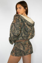 Woman wearing TIC TOC SJ31674-BAYOU BAYOU dark woodland camo fleece mini skort featuring a mid rise elastic waistband with adjustable drawstring, soft lightweight fleece fabric, smooth mini skort silhouette with built-in shorts for coverage, styled with a casual top and sneakers for an easy everyday look.