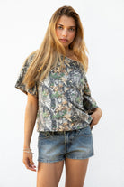 Woman wearing BAYOU camo print oversized one shoulder T-shirt featuring soft washed cotton jersey fabric, oversized slouchy silhouette, asymmetrical neckline, woodland camo print, and loose short sleeves for relaxed off-duty styling.
