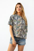 Woman wearing BAYOU camo print oversized one shoulder T-shirt featuring soft washed cotton jersey fabric, oversized slouchy silhouette, asymmetrical neckline, woodland camo print, and loose short sleeves for relaxed off-duty styling.