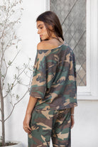 Woman wearing SCOUT military camo short sleeve oversized off shoulder top featuring soft breathable single jersey fabric, allover classic camouflage print, wide rolled raw edge neckline, relaxed oversized silhouette, dropped shoulders, elbow length sleeves, and casual boyfriend inspired draped fit.