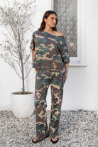 Woman wearing SCOUT military camo short sleeve oversized off shoulder top featuring soft breathable single jersey fabric, allover classic camouflage print, wide rolled raw edge neckline, relaxed oversized silhouette, dropped shoulders, elbow length sleeves, and casual boyfriend inspired draped fit.