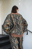 Woman wearing BAYOU dark woodland camo mock neck sweatshirt featuring soft cloud fleece fabric, allover woodland camo print, wide mock neckline with contrast ribbed trim, dropped shoulder relaxed silhouette, oversized fit, long sleeves, and contrast ribbed cuffs and hem.