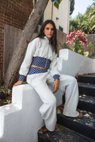 Woman wearing COSETTE polka dot corset waist cropped zip up hoodie featuring soft fleece fabric, contrast navy ribbed corset inspired waistband with allover white polka dot pattern, fitted extended waist, matching polka dot cuffs, full front zipper closure, relaxed drop shoulder sleeves, attached hood, and cropped length designed to coordinate with the matching pants.