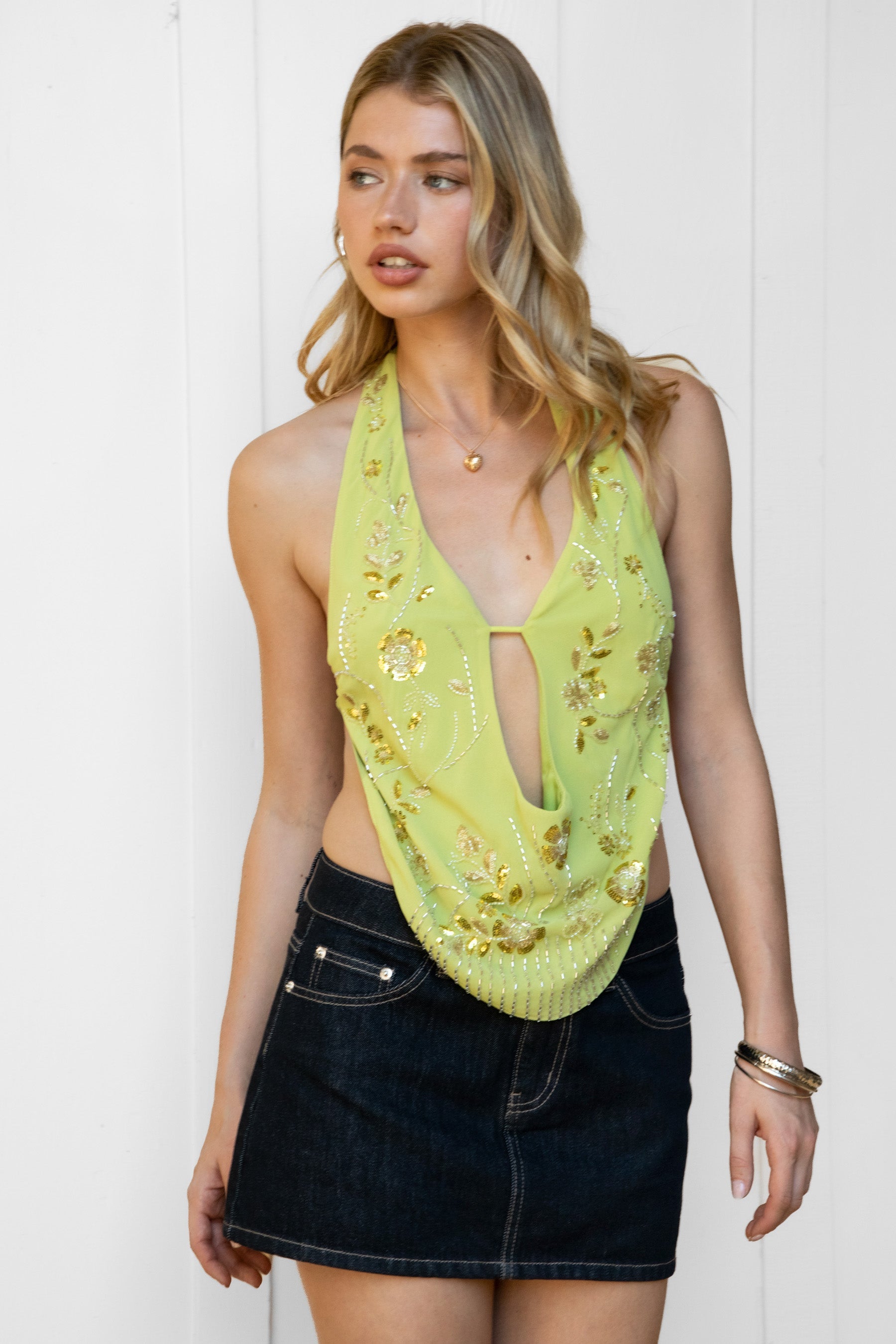 Woman wearing VEDA beaded embroidered cowl halter top featuring a deep draped cowl neckline, halter neck with self tie closure, floral beaded and sequin embroidery at the front, front bust strap detail, open back with adjustable strap, and lightweight sheer chiffon fabric.