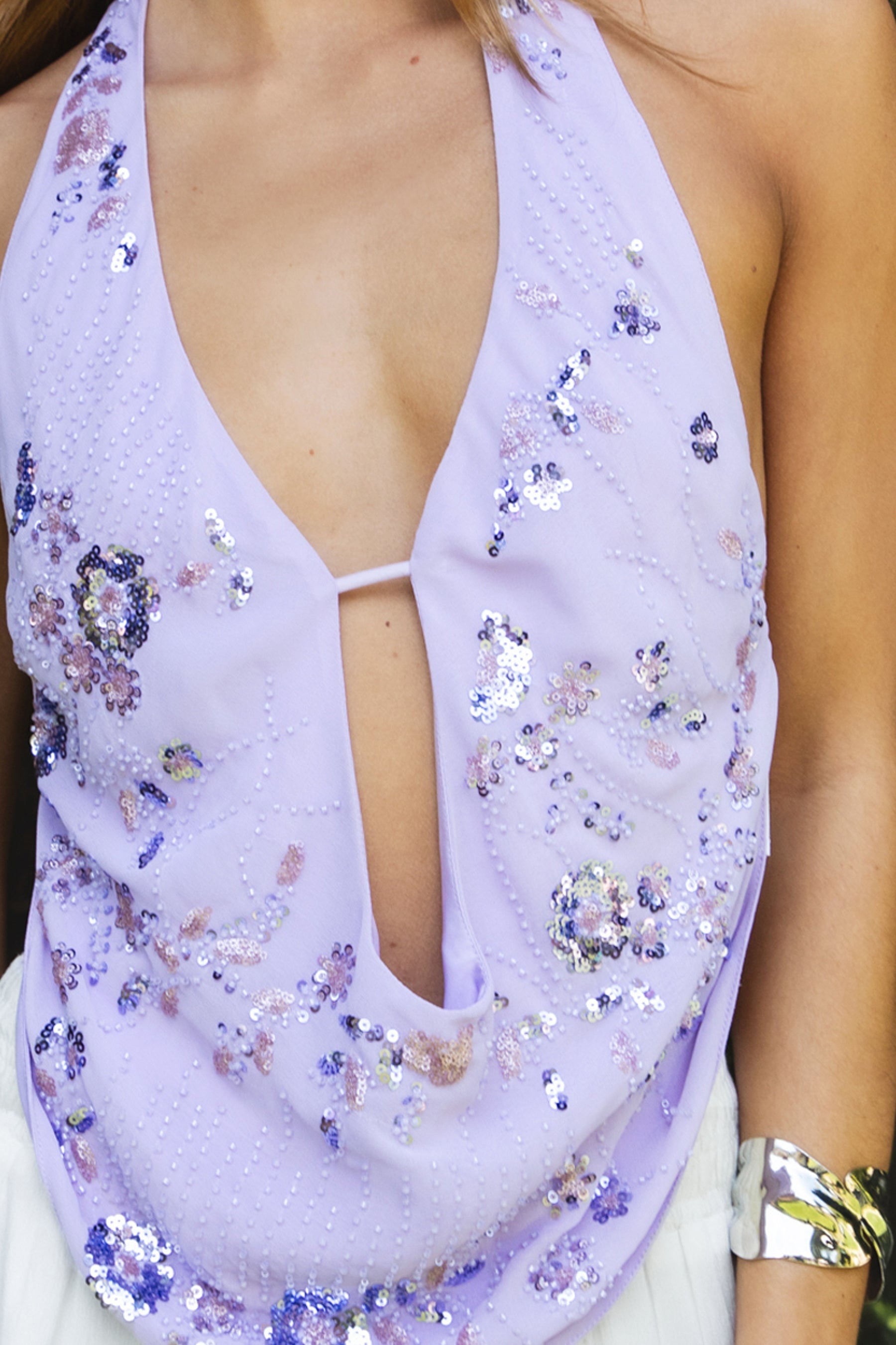 Woman wearing SURA beaded embroidered halter neck top featuring a deep draped cowl neckline, halter neck with self tie closure, floral beaded and sequin embroidery, front bust strap detail, open back with adjustable strap, and lightweight sheer chiffon fabric.