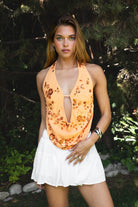Woman wearing SURA beaded embroidered halter neck top featuring a deep draped cowl neckline, halter neck with self tie closure, floral beaded and sequin embroidery, front bust strap detail, open back with adjustable strap, and lightweight sheer chiffon fabric.