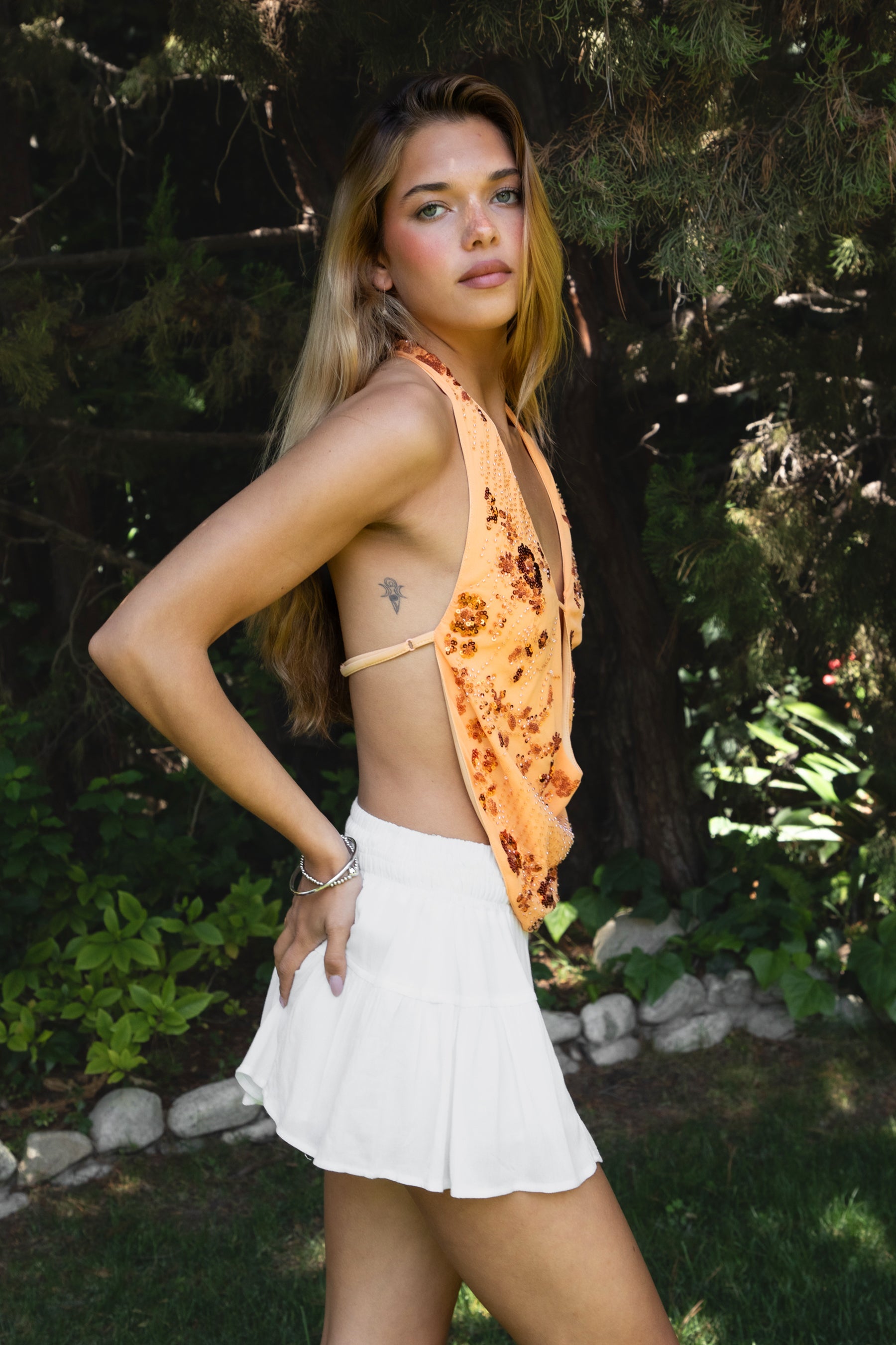 Woman wearing SURA beaded embroidered halter neck top featuring a deep draped cowl neckline, halter neck with self tie closure, floral beaded and sequin embroidery, front bust strap detail, open back with adjustable strap, and lightweight sheer chiffon fabric.