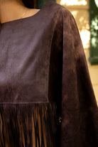 Woman wearing TIC TOC TL31825 STALLION faux suede fringe poncho featuring a cropped cape silhouette, drop shoulder relaxed fit, long fringe tassel detailing along the hem and sleeves, and a soft western-inspired faux suede texture, styled over a fitted top with denim bottoms for a rodeo festival look.