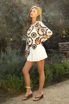 Woman wearing TIC TOC TL31962-SOLANDRA SOLANDRA crochet long sleeve cover up top featuring an open crochet mandala flower pattern in contrast cream and brown circular design, wide round neckline, relaxed easy fit silhouette, and long bell sleeves with lightweight open knit texture, styled over a simple bralette and bottoms for a boho festival and resort-ready look.