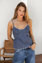 Woman wearing HADLEY plaid check poplin V-neck tank top featuring lightweight cotton poplin fabric, scooped V-neckline with picot trim, faux button detail, adjustable straps, smocked back with tie, and a peplum silhouette with subtle flare.