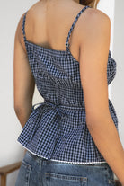Woman wearing HADLEY plaid check poplin V-neck tank top featuring lightweight cotton poplin fabric, scooped V-neckline with picot trim, faux button detail, adjustable straps, smocked back with tie, and a peplum silhouette with subtle flare.