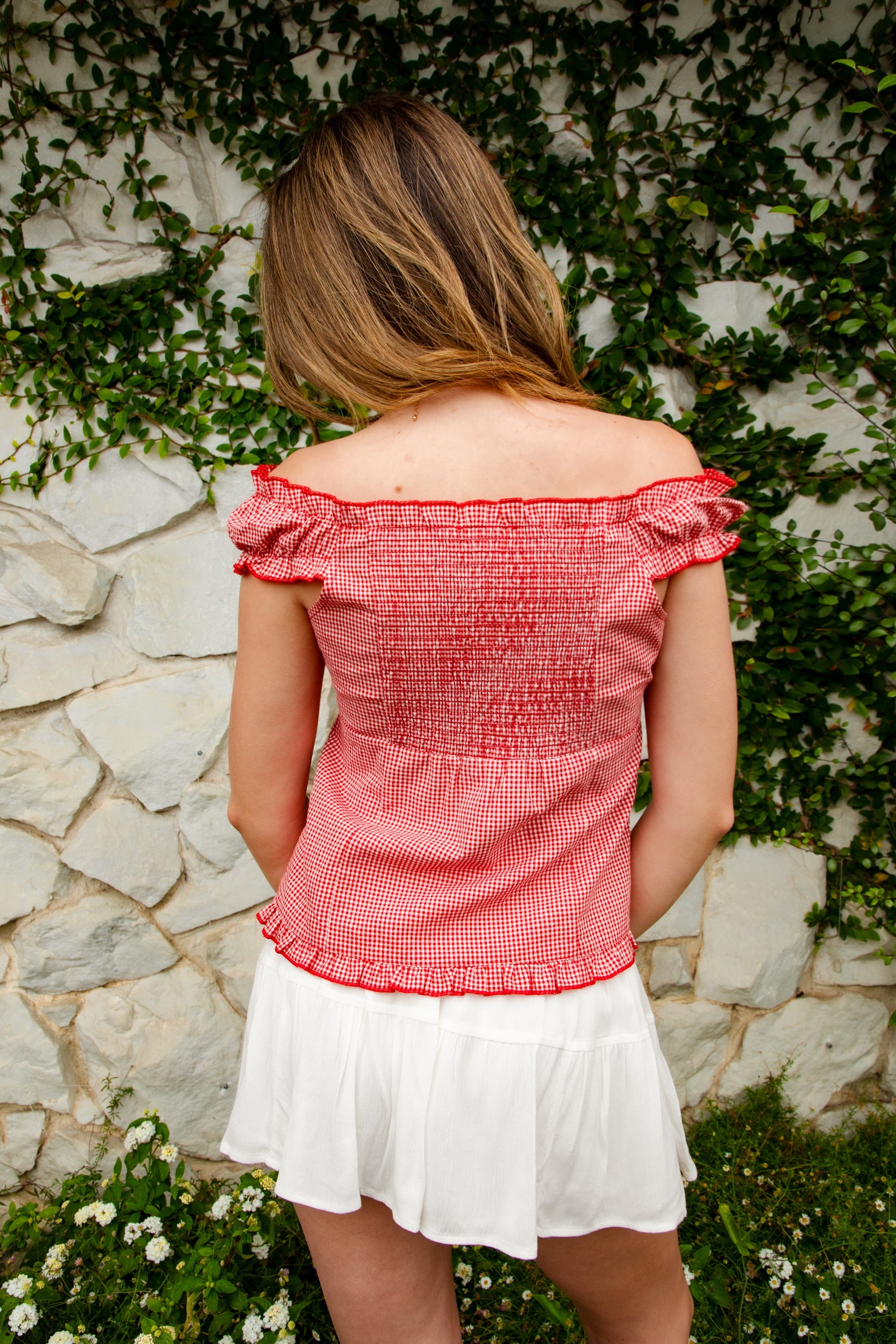 Woman wearing MAREN gingham off shoulder ruffle cap sleeve top featuring a soft ruffle neckline, ruched bust detail, functional button front, smocked back panel, ruffled peplum hem, and lightweight cotton gingham fabric for feminine summer styling.