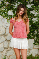 Woman wearing MAREN gingham off shoulder ruffle cap sleeve top featuring a soft ruffle neckline, ruched bust detail, functional button front, smocked back panel, ruffled peplum hem, and lightweight cotton gingham fabric for feminine summer styling.