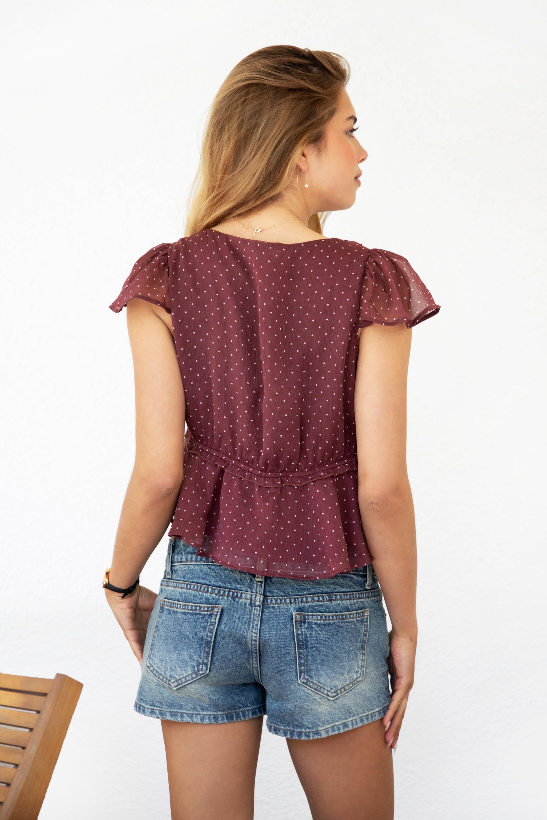 Woman wearing WYNONA polka dot chiffon crop top featuring lightweight printed chiffon, V-neckline with ruffle trim, flutter sleeves, elastic underbust band, front bow detail, and a cropped peplum silhouette with full lining for comfort.