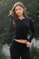 Woman wearing TIC TOC TPA31894-AVELYN AVELYN sweater knit pants set featuring a button front long sleeve ribbed cardigan with a slim cropped silhouette, paired with mid rise knit pants with waistband detail and a relaxed wide leg shape, styled as a cozy matching lounge set for everyday wear.