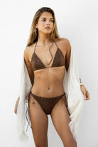 Woman wearing SADDIE suede eyelet laced triangle bikini set featuring a triangle halter top with self tie straps, eyelet lace detailing across the cups and waistband, high cut side strap bottoms, and a soft stretch fabric with suede look finish and fully lined interior.