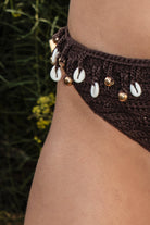 Woman wearing TIC TOC TPC31675-CORALIE CORALIE crochet bikini set featuring a crochet triangle bikini top with seashell and gold charm trim, adjustable halter neck and back self ties, and a matching high cut bikini bottom with cheeky coverage, styled barefoot by the pool for a relaxed beach vacation look.