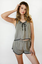 Woman wearing PRAIRELLE gingham embroidered sleeveless top and shorts set featuring a sweet gingham print, delicate floral embroidery lace trim, front self tie bow detail, matching elastic waist shorts, scalloped lace hem, and lightweight rayon fabric for relaxed summer styling.
