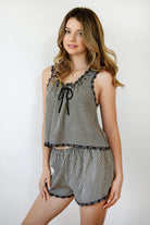 Woman wearing PRAIRELLE gingham embroidered sleeveless top and shorts set featuring a sweet gingham print, delicate floral embroidery lace trim, front self tie bow detail, matching elastic waist shorts, scalloped lace hem, and lightweight rayon fabric for relaxed summer styling.