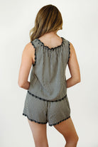 Woman wearing PRAIRELLE gingham embroidered sleeveless top and shorts set featuring a sweet gingham print, delicate floral embroidery lace trim, front self tie bow detail, matching elastic waist shorts, scalloped lace hem, and lightweight rayon fabric for relaxed summer styling.