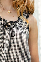 Woman wearing PRAIRELLE gingham embroidered sleeveless top and shorts set featuring a sweet gingham print, delicate floral embroidery lace trim, front self tie bow detail, matching elastic waist shorts, scalloped lace hem, and lightweight rayon fabric for relaxed summer styling.