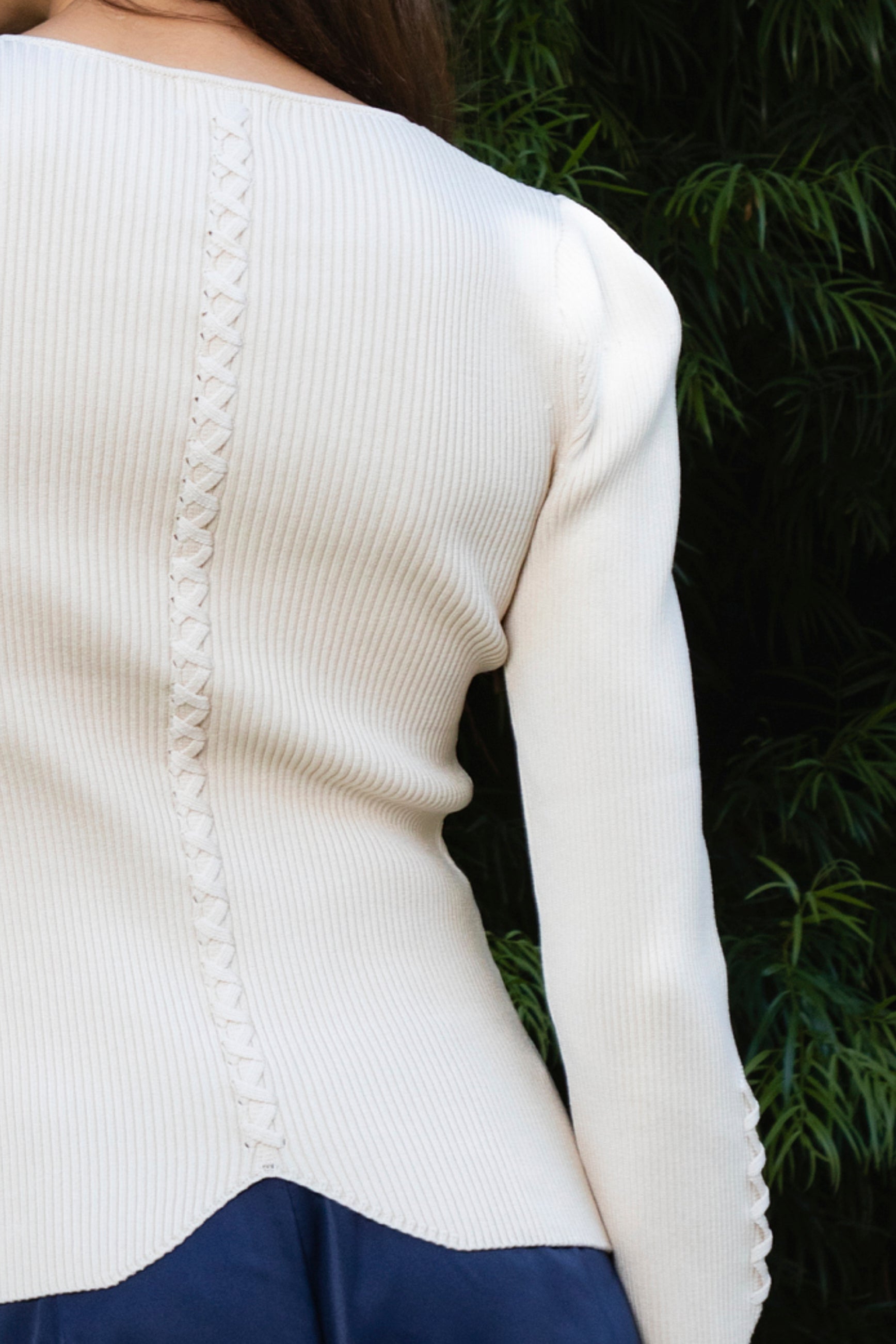 Woman wearing VIVIENNE lace up ribbed knit cardigan featuring fitted ribbed sweater knit fabric, soft scoop neckline, covered button front closure, long sleeves with subtle puff shoulder shaping, lace up detailing along the sleeve cuffs, decorative lace up detail down the center back, and slightly curved hem with fitted waist shaping.