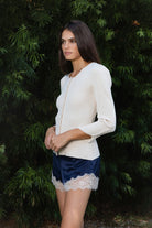 Woman wearing VIVIENNE lace up ribbed knit cardigan featuring fitted ribbed sweater knit fabric, soft scoop neckline, covered button front closure, long sleeves with subtle puff shoulder shaping, lace up detailing along the sleeve cuffs, decorative lace up detail down the center back, and slightly curved hem with fitted waist shaping.