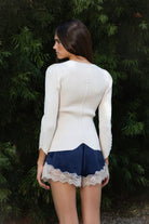 Woman wearing VIVIENNE lace up ribbed knit cardigan featuring fitted ribbed sweater knit fabric, soft scoop neckline, covered button front closure, long sleeves with subtle puff shoulder shaping, lace up detailing along the sleeve cuffs, decorative lace up detail down the center back, and slightly curved hem with fitted waist shaping.