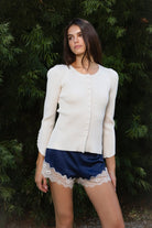 Woman wearing VIVIENNE lace up ribbed knit cardigan featuring fitted ribbed sweater knit fabric, soft scoop neckline, covered button front closure, long sleeves with subtle puff shoulder shaping, lace up detailing along the sleeve cuffs, decorative lace up detail down the center back, and slightly curved hem with fitted waist shaping.