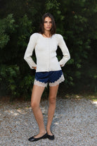 Woman wearing VIVIENNE lace up ribbed knit cardigan featuring fitted ribbed sweater knit fabric, soft scoop neckline, covered button front closure, long sleeves with subtle puff shoulder shaping, lace up detailing along the sleeve cuffs, decorative lace up detail down the center back, and slightly curved hem with fitted waist shaping.