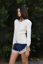 Woman wearing VIVIENNE lace up ribbed knit cardigan featuring fitted ribbed sweater knit fabric, soft scoop neckline, covered button front closure, long sleeves with subtle puff shoulder shaping, lace up detailing along the sleeve cuffs, decorative lace up detail down the center back, and slightly curved hem with fitted waist shaping.