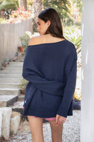 Woman wearing LOBELLE lobster graphic off shoulder sweater featuring relaxed sweater knit fabric, bold contrast red lobster intarsia graphic at the front, wide neckline designed to drape off the shoulder, oversized slouchy silhouette, dropped shoulders, long relaxed sleeves, ribbed cuffs and hem, and subtle side slits.