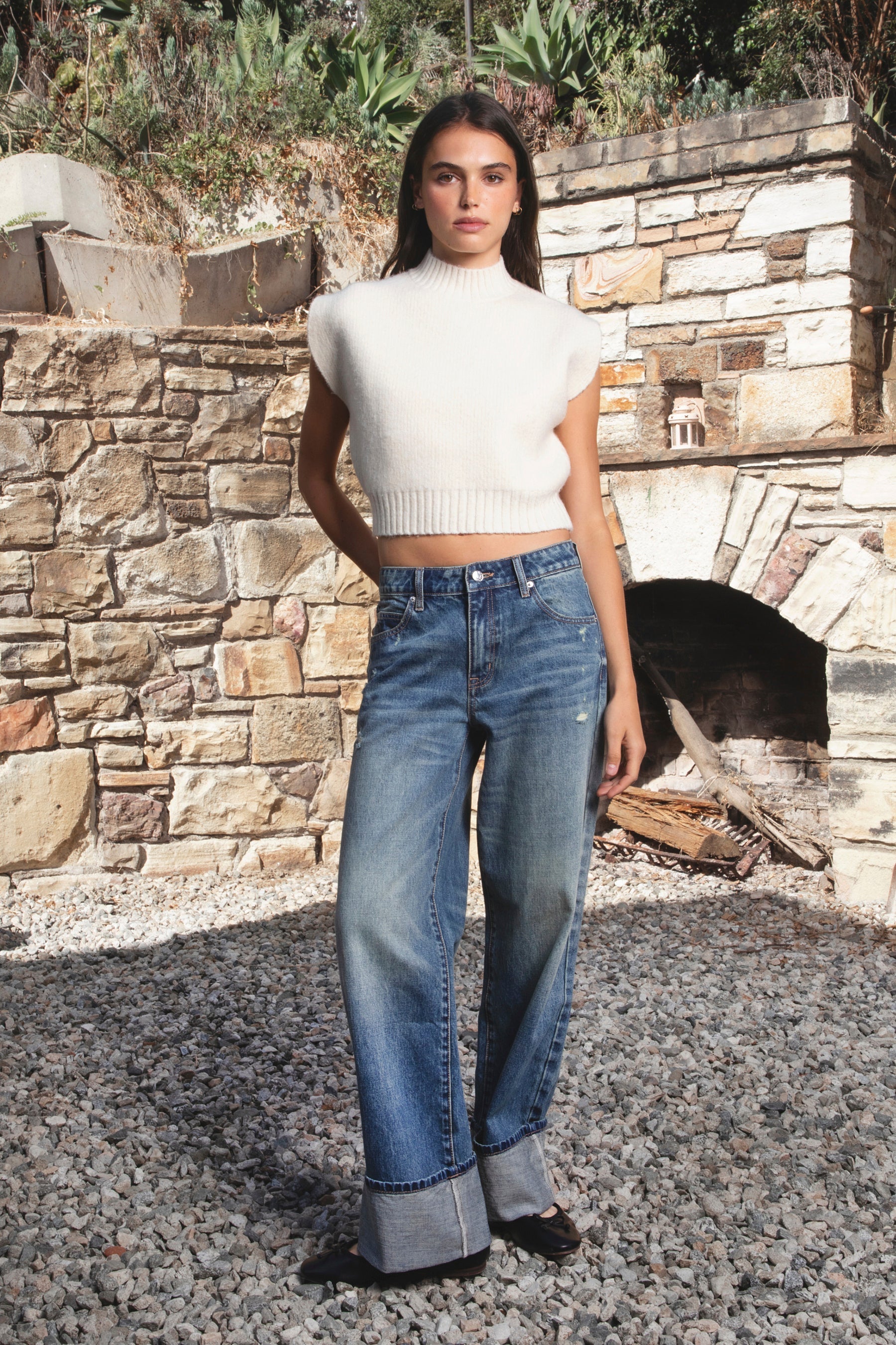 Woman wearing GARANCE mock neck sleeveless sweater top featuring a soft fuzzy knit texture, clean minimalist silhouette, polished mock neckline, relaxed bodice, subtle extended shoulder design, cropped length, wide ribbed hem, and solid color design for easy transitional layering.