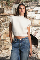 Woman wearing GARANCE mock neck sleeveless sweater top featuring a soft fuzzy knit texture, clean minimalist silhouette, polished mock neckline, relaxed bodice, subtle extended shoulder design, cropped length, wide ribbed hem, and solid color design for easy transitional layering.