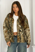 Woman wearing TIC TOC TT31858-LAUREL LAUREL oversized corduroy collar camo jacket featuring an allover wild camo print canvas twill body, contrast corduroy collar, front zipper closure, front two pockets, drop shoulder oversized fit, and satin quilted lining, styled with denim and a simple top for a western streetwear-inspired everyday look.