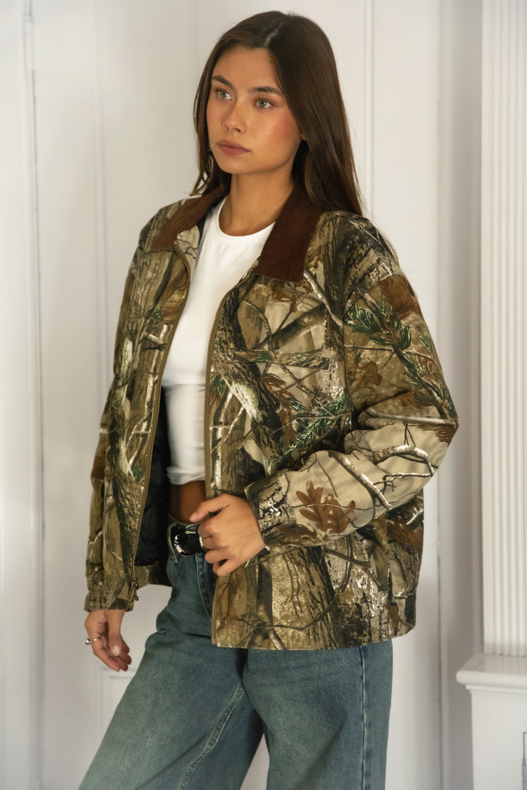 Woman wearing TIC TOC TT31858-LAUREL LAUREL oversized corduroy collar camo jacket featuring an allover wild camo print canvas twill body, contrast corduroy collar, front zipper closure, front two pockets, drop shoulder oversized fit, and satin quilted lining, styled with denim and a simple top for a western streetwear-inspired everyday look.