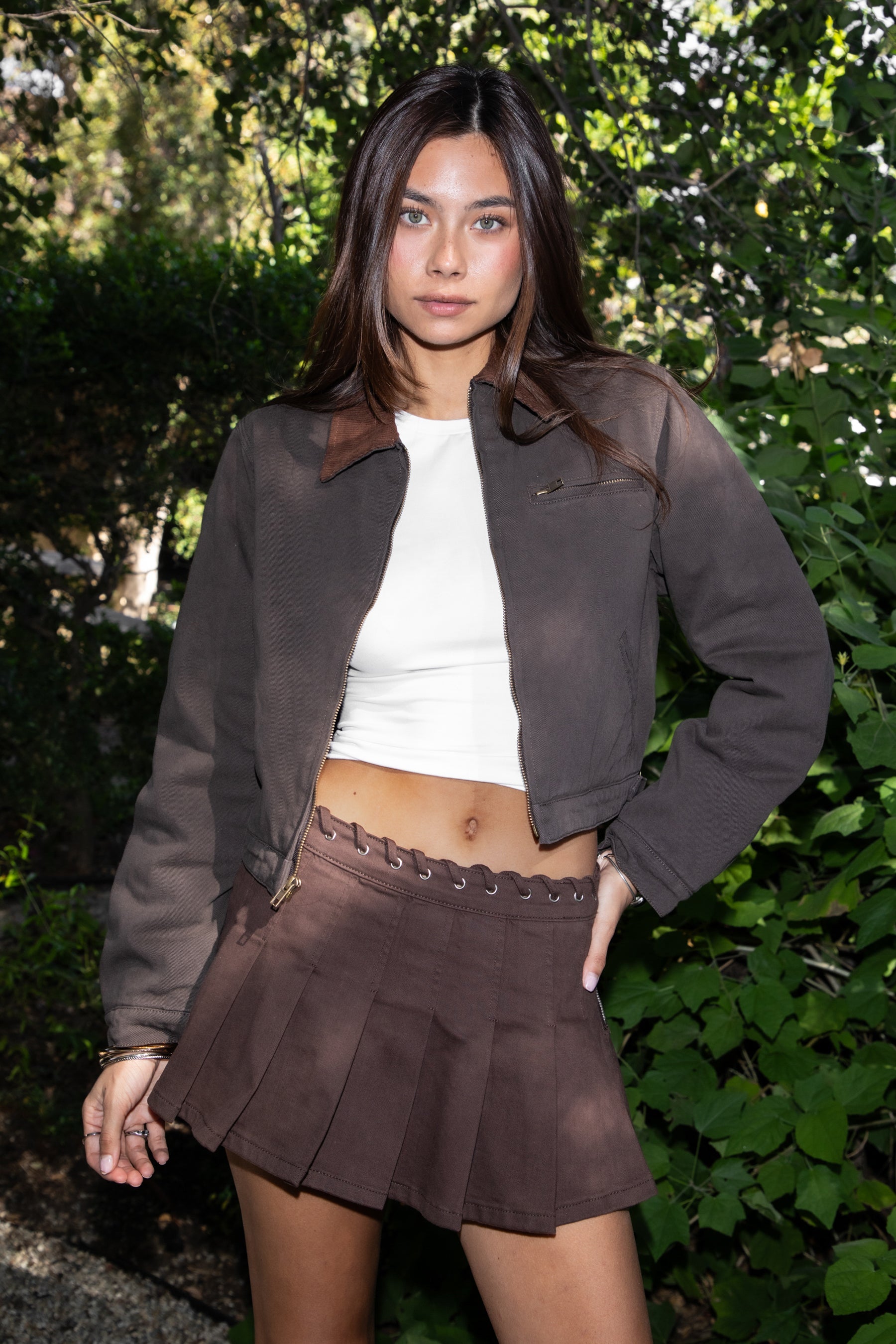 Woman wearing TIC TOC TT31861-FLINT FLINT washed solid twill cropped jacket featuring a front zip closure, contrast brown corduroy collar, two side pockets, a single chest zip pocket, snap button cuffs, and side buckle strap detail at the waistline, with satin quilted lining and light padding, styled over a simple top and denim for a western-inspired everyday transitional look.