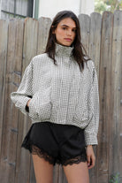Woman wearing MARGOT plaid gingham zip up bomber jacket featuring lightweight crinkled cotton blend fabric, classic gingham plaid pattern, high neck collar, front button and zip closure, semi cropped length, sleeve snap buttons, relaxed drop shoulder silhouette, side pockets, and elastic hem.