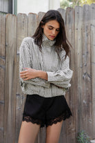 Woman wearing MARGOT plaid gingham zip up bomber jacket featuring lightweight crinkled cotton blend fabric, classic gingham plaid pattern, high neck collar, front button and zip closure, semi cropped length, sleeve snap buttons, relaxed drop shoulder silhouette, side pockets, and elastic hem.