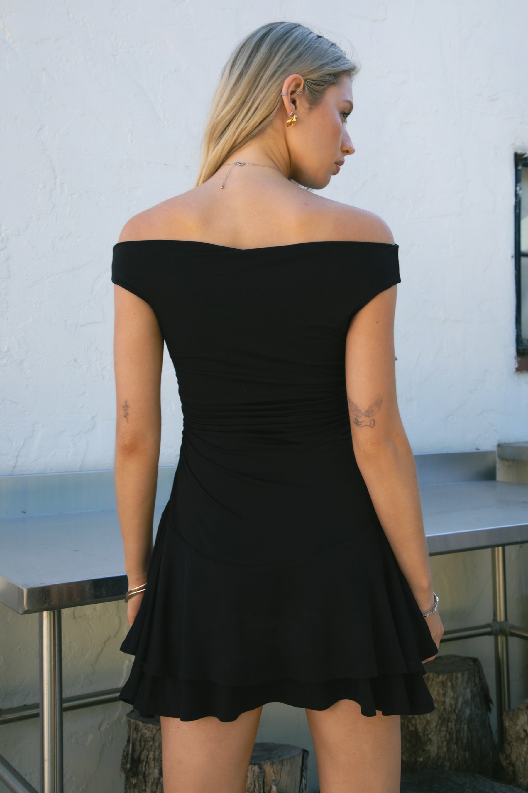 Woman wearing TIC TOC DC31642BA RAVAYA off-the-shoulder mini dress featuring ruched sides and a frill hemline in soft rayon spandex fabric