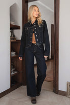 Woman wearing TIC TOC PF31703 MILLS selvedge denim straight leg pants in dark blue wash with a low-rise waist and wide-leg silhouette with a matching jackte in an indoor setting. 