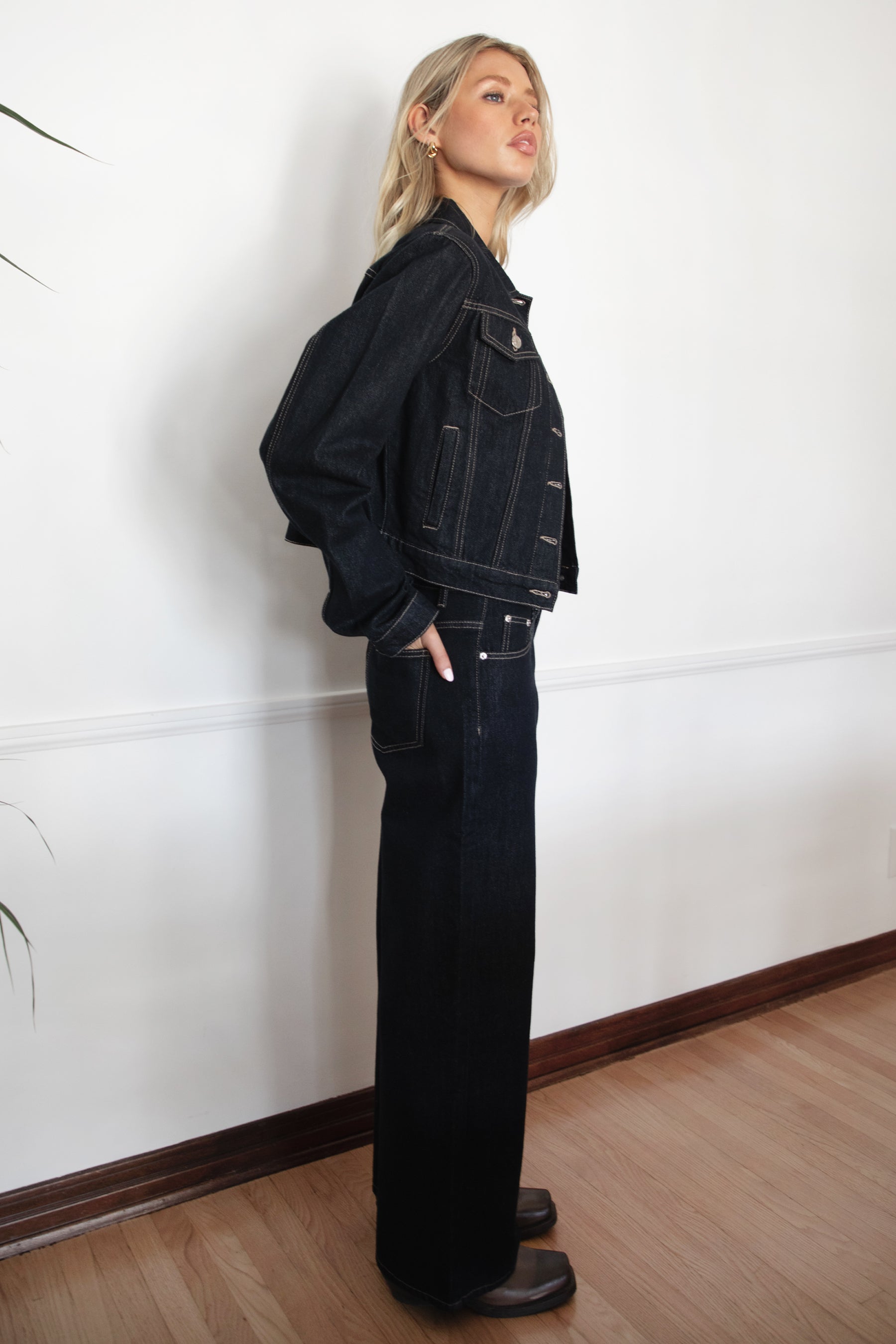 Woman wearing TIC TOC PF31703 MILLS selvedge denim straight leg pants in dark blue wash with a low-rise waist and wide-leg silhouette with a matching jackte in an indoor setting. 