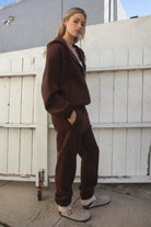Person wearing a brown tracksuit and white crop top in front of a white wooden door.