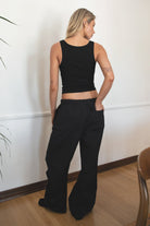 Woman wearing TIC TOC PH28246 GENIE black parachute twill pants featuring adjustable waistband, relaxed wide-leg fit, and drawstring hems. against a white wall.