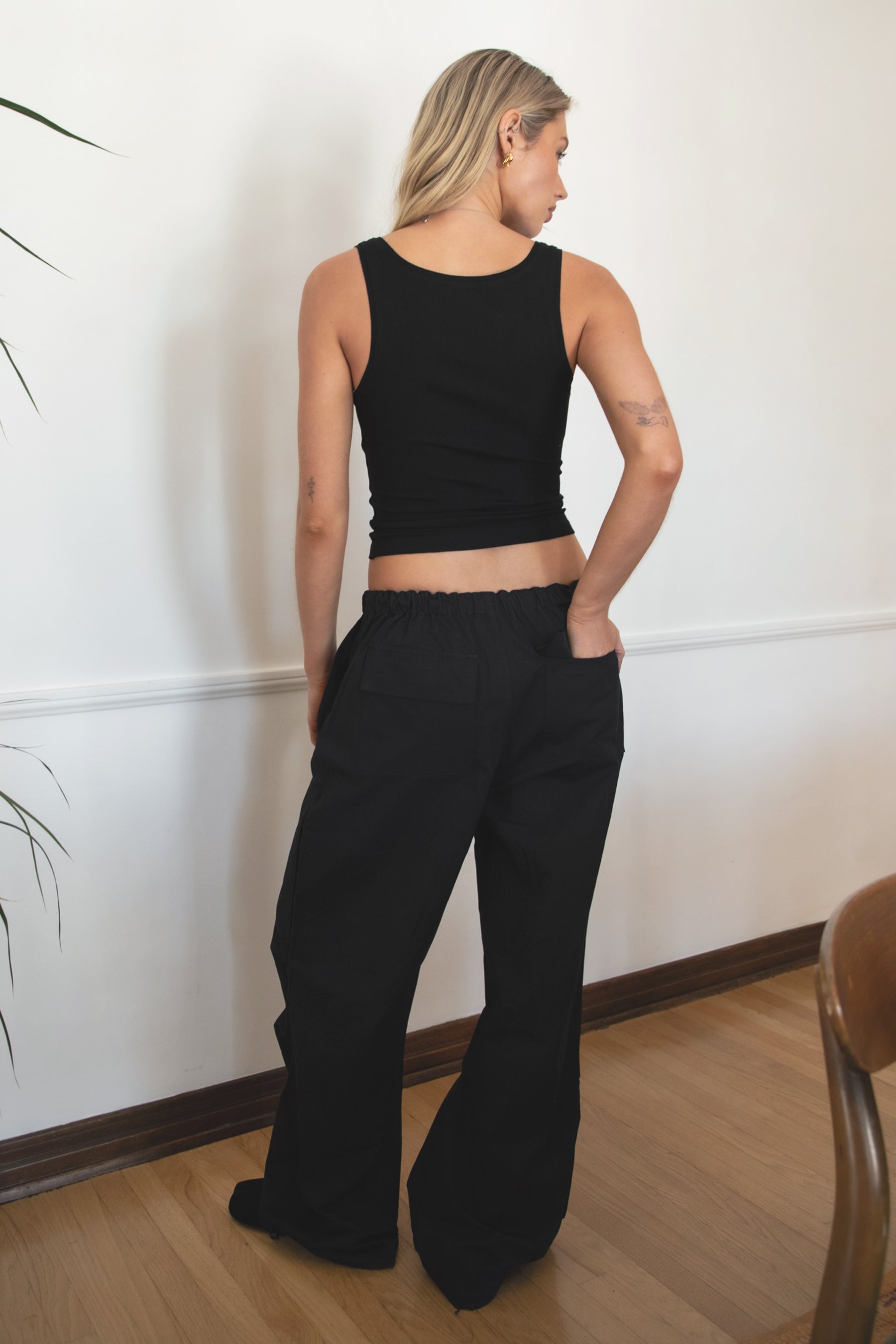 Woman wearing TIC TOC PH28246 GENIE black parachute twill pants featuring adjustable waistband, relaxed wide-leg fit, and drawstring hems. against a white wall.