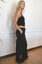 Woman wearing TIC TOC PH28246 GENIE black parachute twill pants featuring adjustable waistband, relaxed wide-leg fit, and drawstring hems. against a white wall.