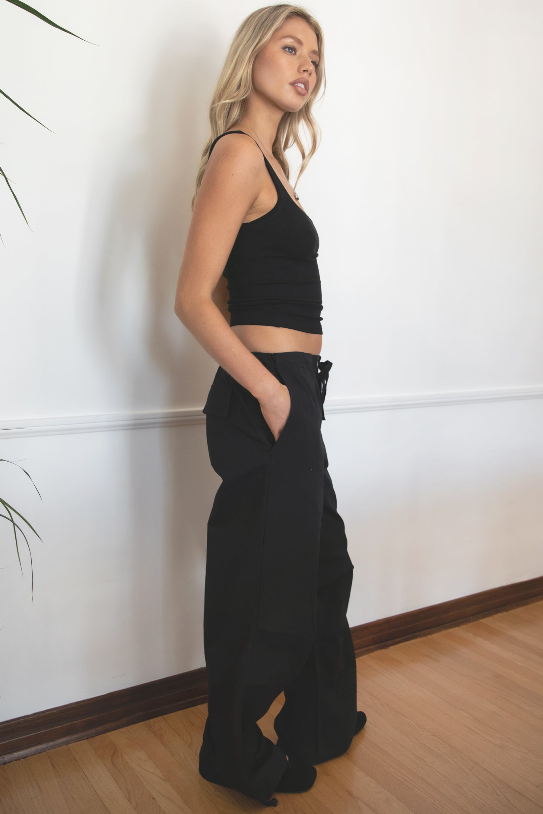 Woman wearing TIC TOC PH28246 GENIE black parachute twill pants featuring adjustable waistband, relaxed wide-leg fit, and drawstring hems. against a white wall.