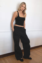 Woman wearing TIC TOC PH28246 GENIE black parachute twill pants featuring adjustable waistband, relaxed wide-leg fit, and drawstring hems. against a white wall.