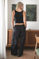 Woman wearing a black tank top and TIC TOC PH29131 TOMY black crinkled nylon parachute cargo pants with adjustable drawstring waistband and wide-leg silhouette indoors
