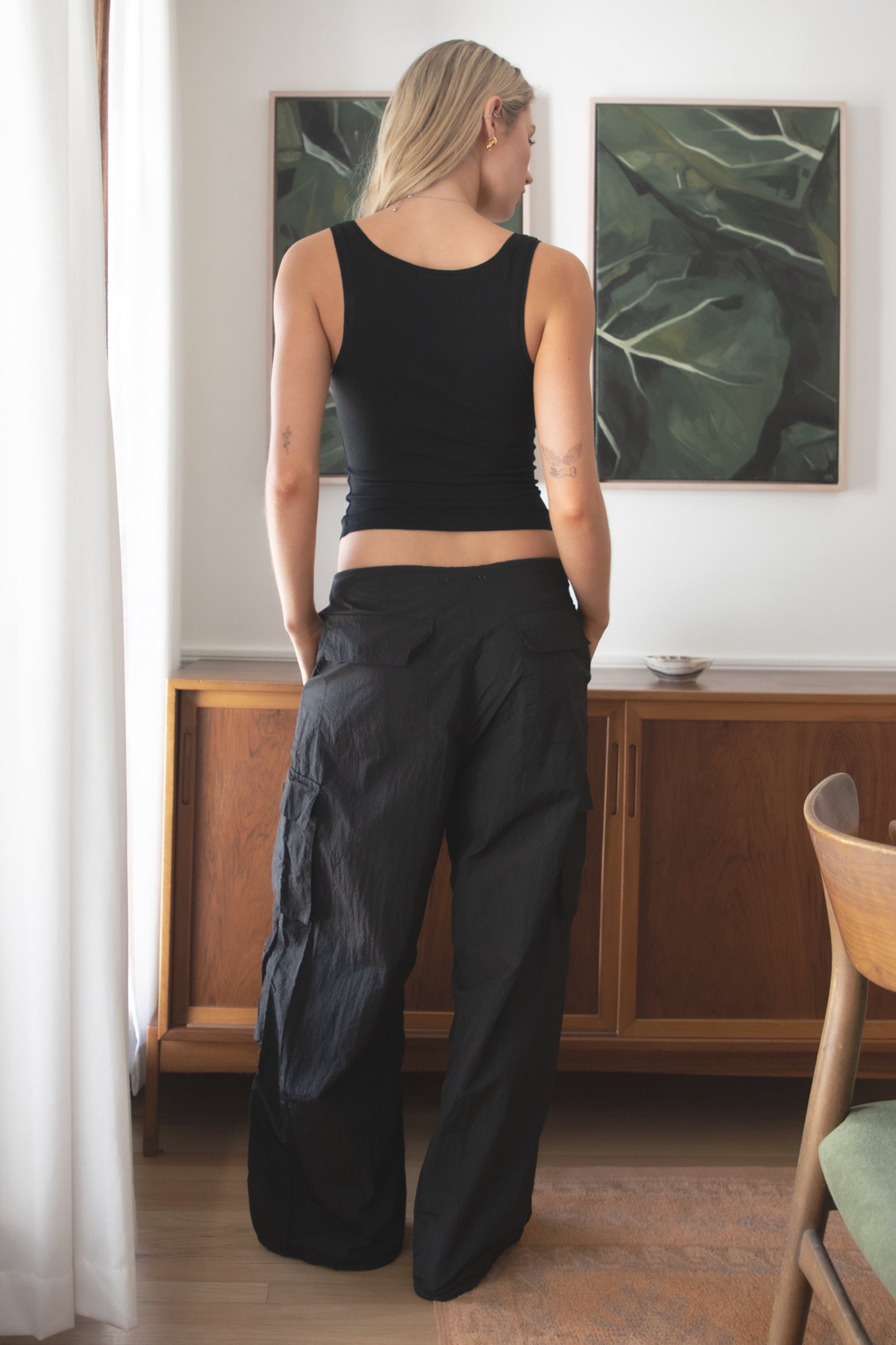 Woman wearing a black tank top and TIC TOC PH29131 TOMY black crinkled nylon parachute cargo pants with adjustable drawstring waistband and wide-leg silhouette indoors